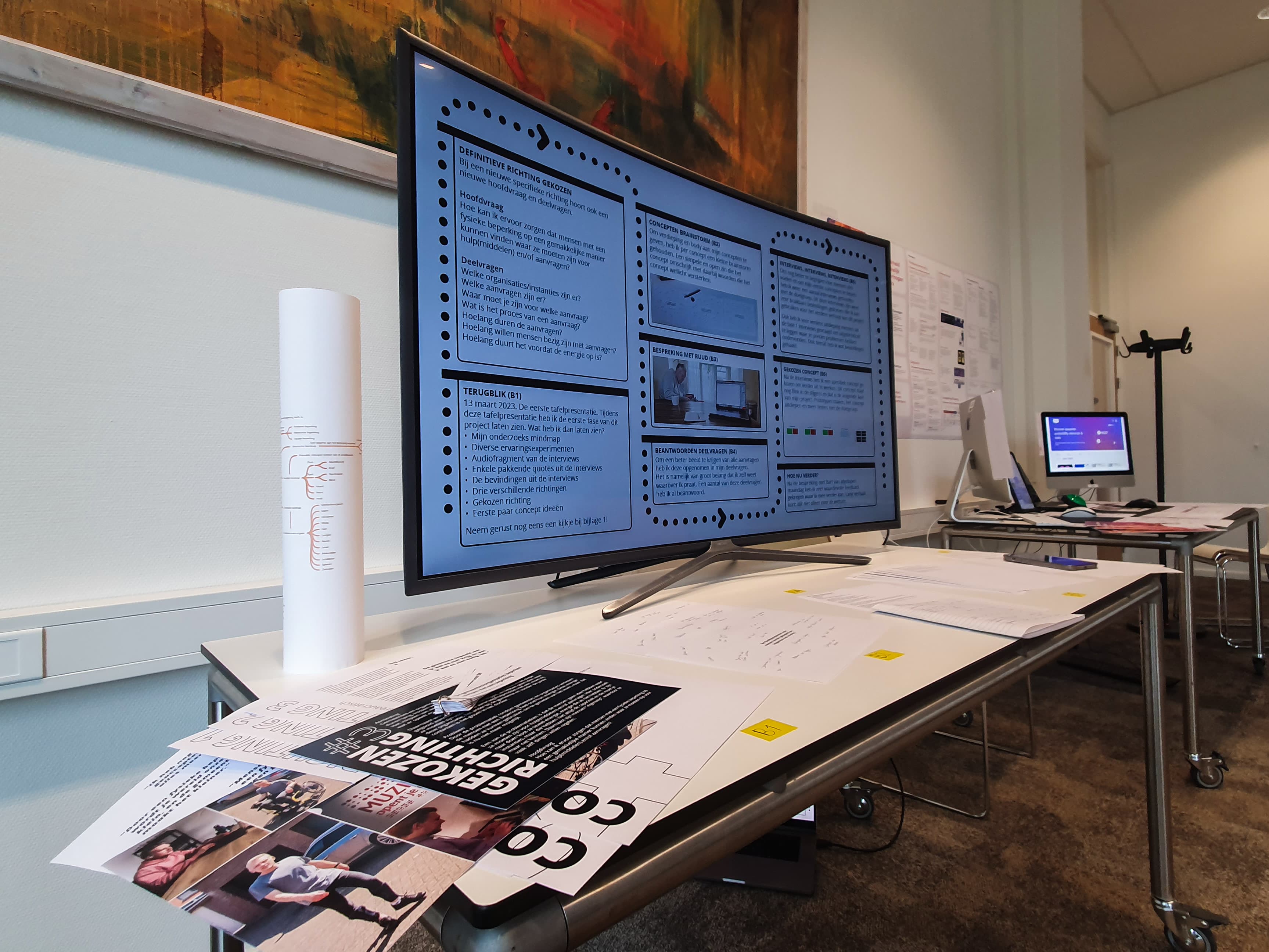 Een foto van de expositie die Rick Marcelissen heeft neergelegd tijdens de tweede tafelpresentatie. Een groot tv-scherm toont een infographic van de stappen die Rick heeft gezet en op de tafel liggen ondersteunende documenten.